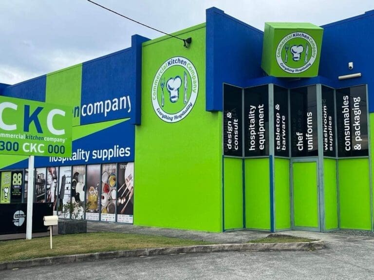 Vibrant green and blue storefront of a commercial kitchen equipment company, featuring large glass windows and various services like design, equipment, consumables, and uniforms advertised on the facade.